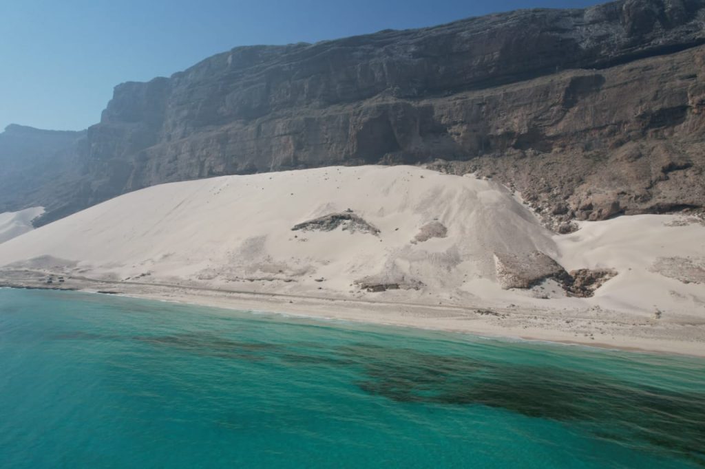Towering white dunes meeting turquoise sea beneath the cliffs of Socotra
