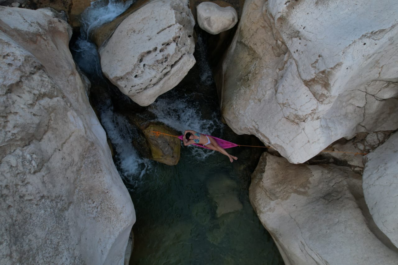 Traveller resting in a hammock above a wadi pool between giant boulders